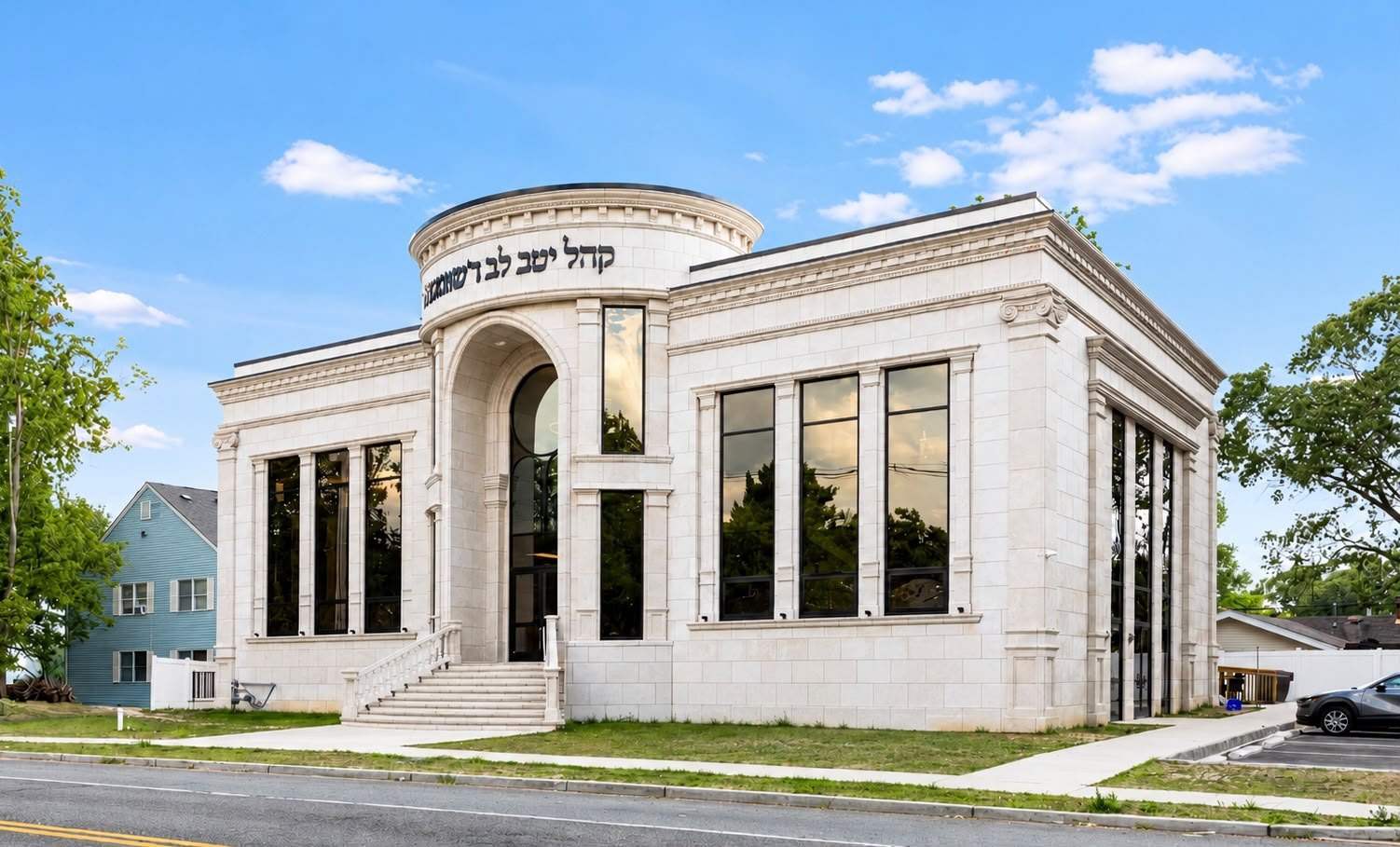 Stone shul with an arched entry, a round drum and tall black windows, under a blue sky
